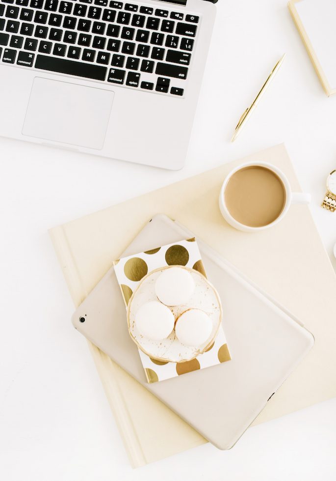 Female home office workspace with laptop, sweets, coffee, feminine accessories. Flat lay, top view gold bright modern background.